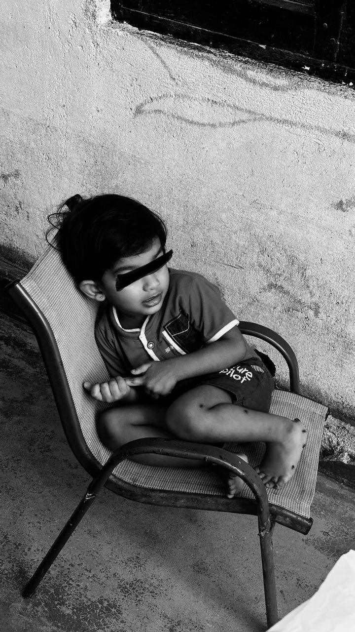 Black-and-white photo of a small child sitting in a metal chair at home