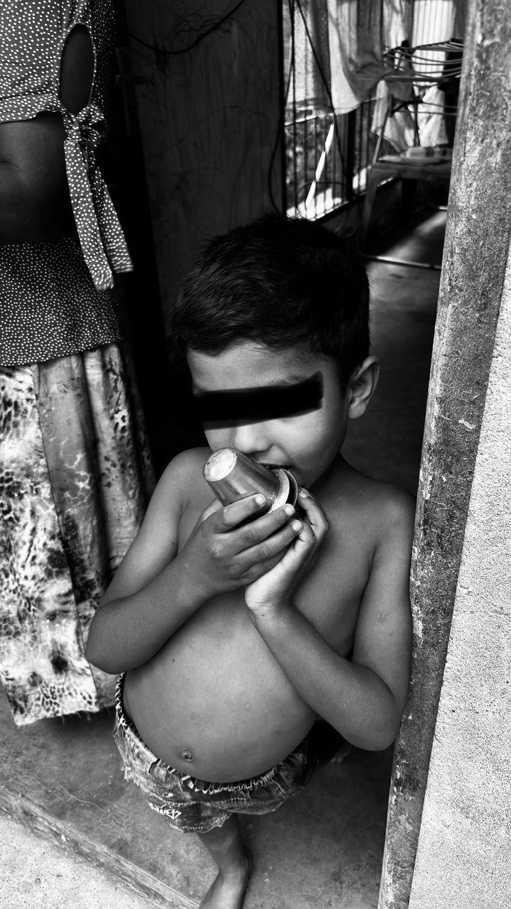 Black-and-white photo of a young boy holding a steel cup to his mouth