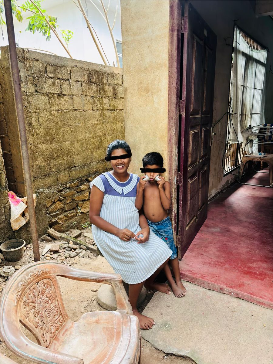 A smiling expectant mother sitting outside her home with a young boy